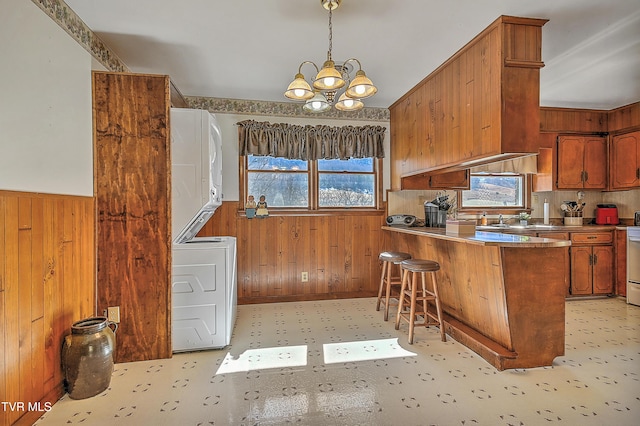 kitchen with wooden walls, stacked washing maching and dryer, wainscoting, and brown cabinets