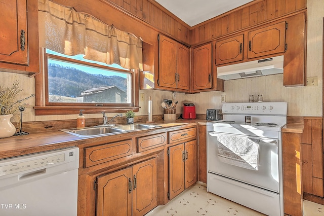 kitchen featuring brown cabinetry, white appliances, a sink, and under cabinet range hood