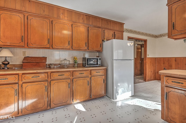 kitchen featuring brown cabinetry, freestanding refrigerator, and wainscoting