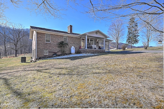 view of front facade with a front yard, a chimney, a porch, and brick siding