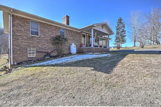 rear view of house featuring covered porch, a yard, brick siding, and a chimney