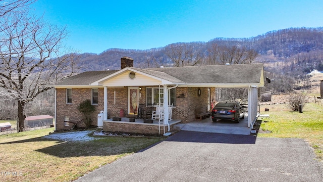 view of front of home with a chimney, aphalt driveway, a front lawn, a porch, and brick siding