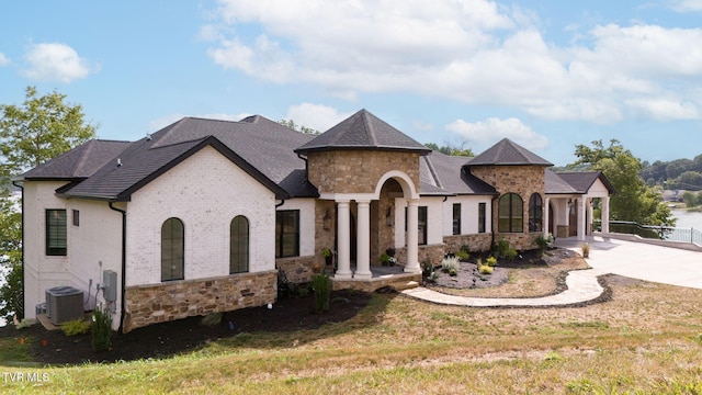 french country home featuring stone siding, concrete driveway, a front lawn, and central AC unit