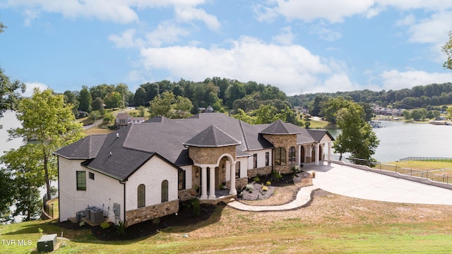 view of front facade featuring driveway, a garage, stone siding, a water view, and fence