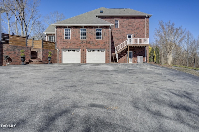 view of home's exterior featuring driveway, central AC, an attached garage, brick siding, and stairs