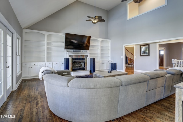 living room with a fireplace with raised hearth, baseboards, a ceiling fan, and dark wood-style flooring