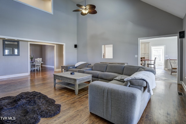 living room featuring visible vents, ceiling fan, baseboards, a towering ceiling, and wood finished floors