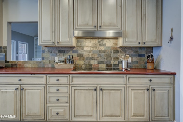 kitchen with under cabinet range hood, decorative backsplash, black electric stovetop, and dark countertops