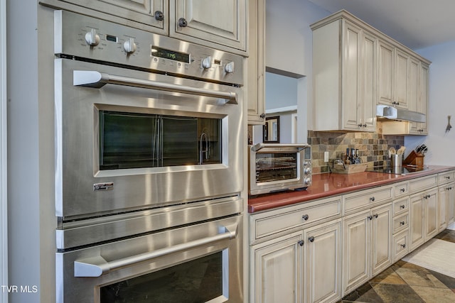 kitchen with cream cabinetry, under cabinet range hood, tasteful backsplash, double oven, and black electric cooktop