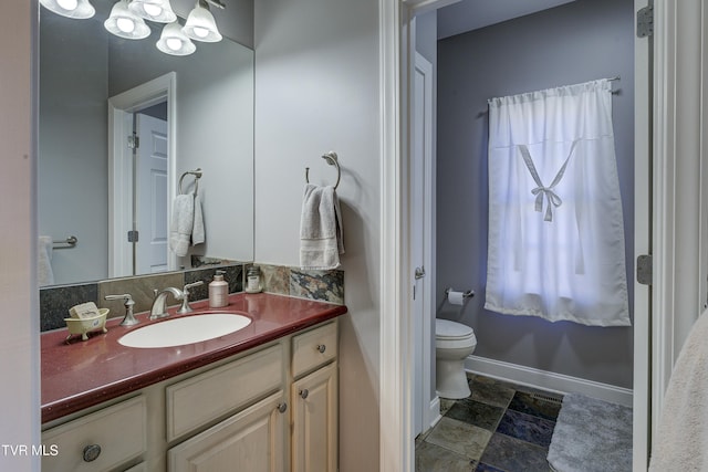 bathroom featuring vanity, toilet, baseboards, and stone finish flooring