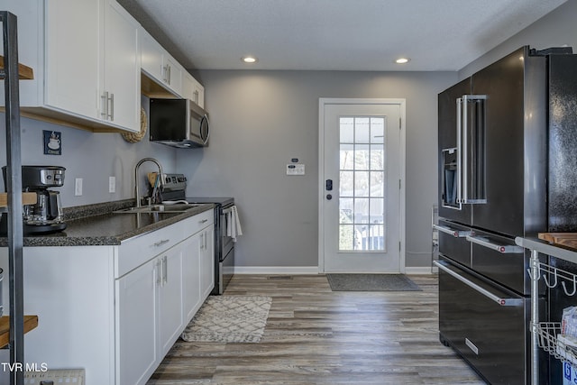 kitchen with a sink, light wood-style floors, appliances with stainless steel finishes, white cabinetry, and dark countertops