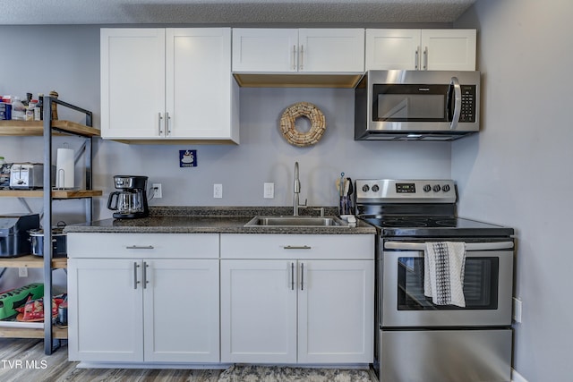 kitchen with wood finished floors, dark stone counters, a sink, white cabinets, and appliances with stainless steel finishes