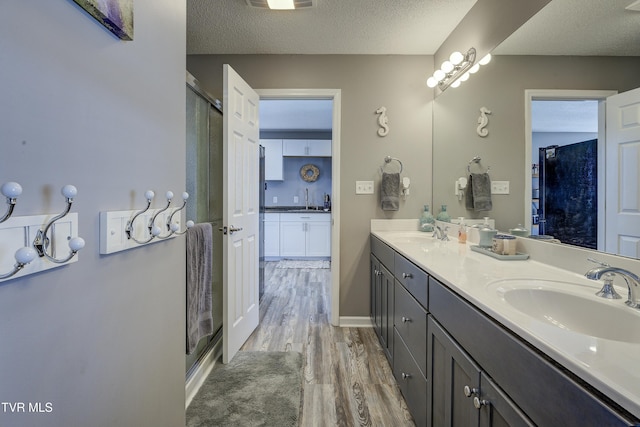 full bathroom featuring wood finished floors, double vanity, a sink, a shower stall, and a textured ceiling