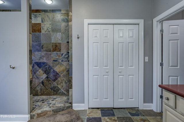 bathroom featuring stone finish floor, a closet, baseboards, walk in shower, and vanity