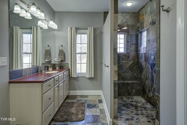 full bathroom featuring baseboards, stone tile flooring, vanity, and a walk in shower