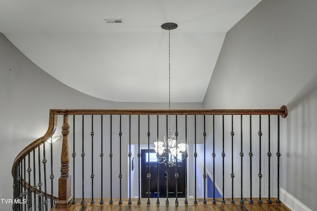 staircase with an inviting chandelier, wood finished floors, visible vents, and vaulted ceiling