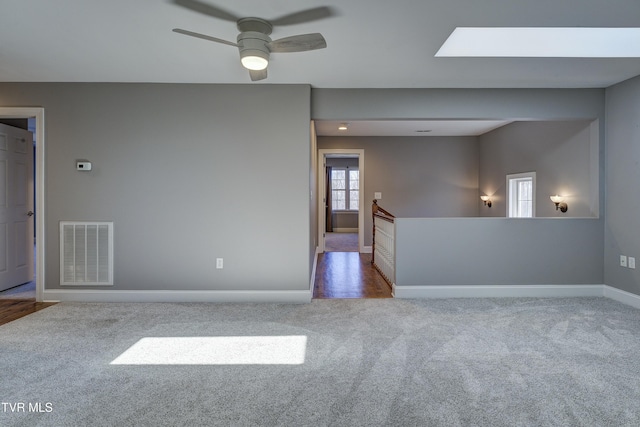 carpeted empty room featuring visible vents, a skylight, baseboards, and a ceiling fan