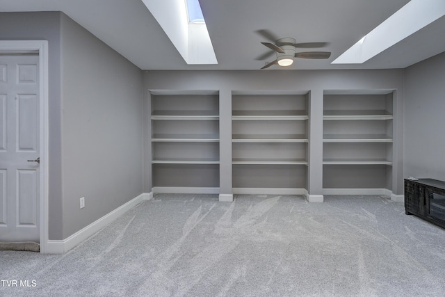 interior space featuring baseboards, built in features, carpet floors, a skylight, and a ceiling fan