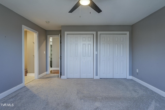 unfurnished bedroom with a ceiling fan, carpet, baseboards, and two closets