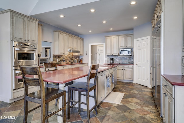 kitchen featuring cream cabinetry, stone finish floor, stainless steel appliances, and a sink