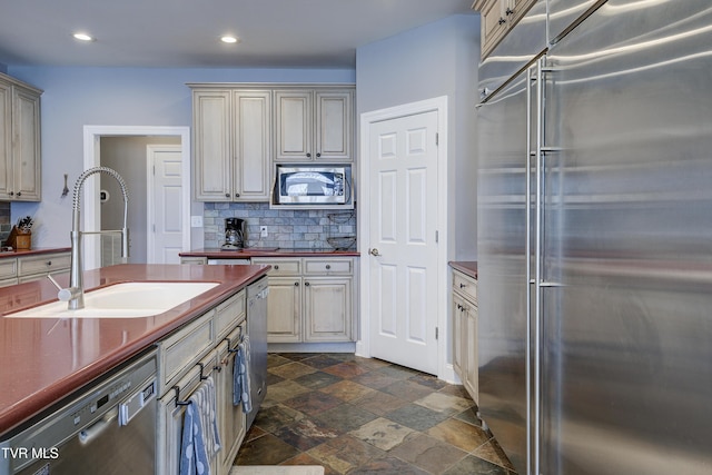 kitchen with tasteful backsplash, stone finish flooring, built in appliances, cream cabinets, and a sink