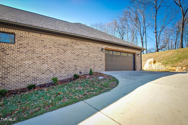 view of property exterior with an attached garage, driveway, a shingled roof, and brick siding