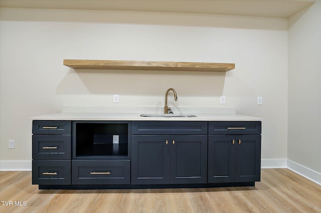 bar with light wood finished floors, a sink, and baseboards