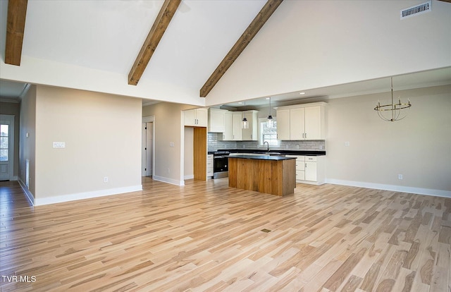 kitchen with backsplash, an inviting chandelier, gas stove, a kitchen island, and beamed ceiling