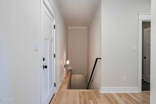 hallway with baseboards, ornamental molding, wood finished floors, and an upstairs landing