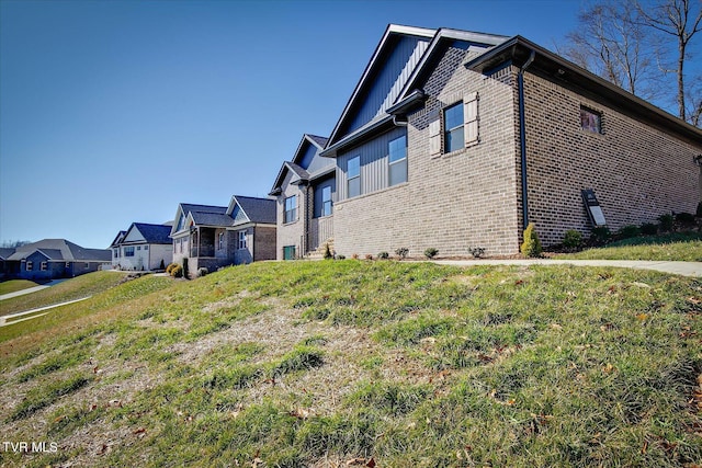 view of side of home with board and batten siding, a residential view, a lawn, and brick siding