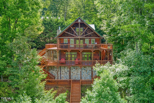 back of house with faux log siding, a wooded view, a wooden deck, and stairs