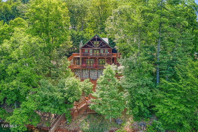 view of front facade with a balcony, a forest view, and a chimney