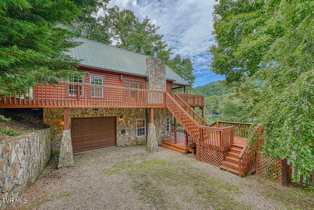 back of property with driveway, stone siding, stairway, an attached garage, and a deck