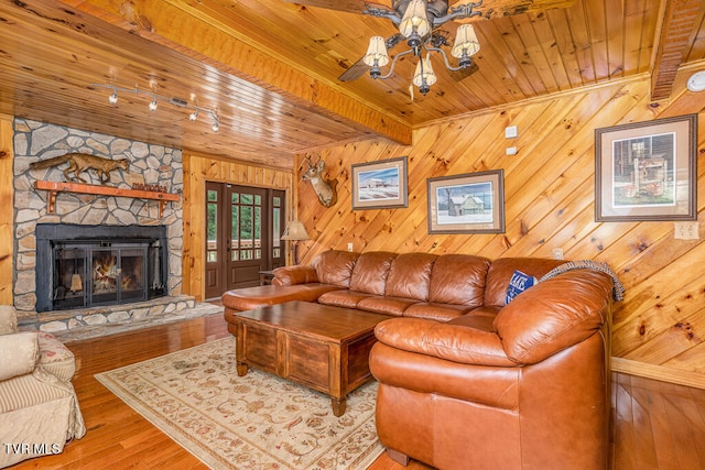 living room featuring light wood-style flooring, wooden ceiling, beamed ceiling, and a stone fireplace