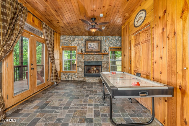 rec room featuring a ceiling fan, wood ceiling, a stone fireplace, and french doors