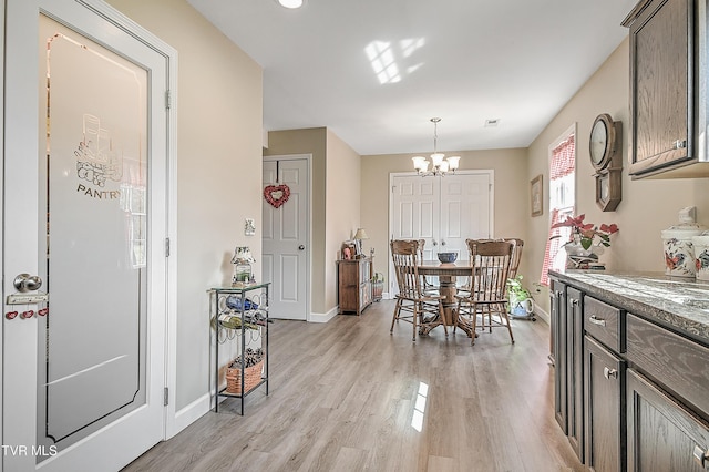 dining space featuring light wood-style flooring, baseboards, and an inviting chandelier