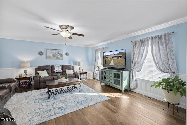 living room with a ceiling fan, wainscoting, crown molding, and wood finished floors