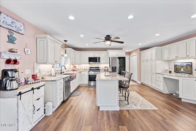 kitchen with light wood-style flooring, appliances with stainless steel finishes, white cabinets, built in study area, and a kitchen bar