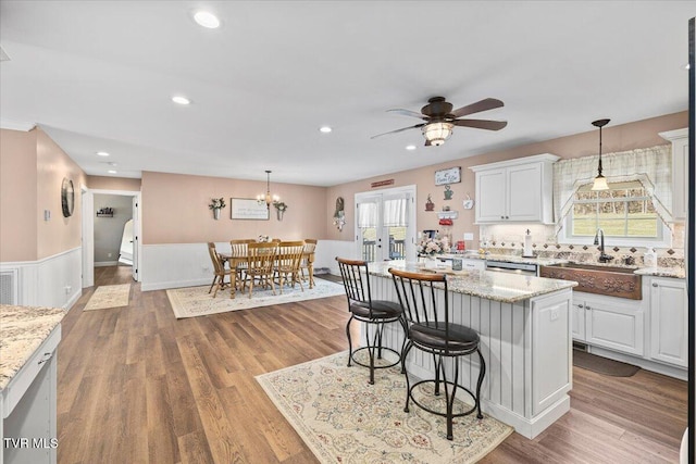 kitchen featuring a breakfast bar area, recessed lighting, white cabinetry, a sink, and wood finished floors