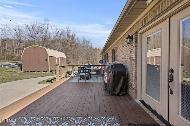 deck with a storage shed, outdoor dining area, an outbuilding, and a grill