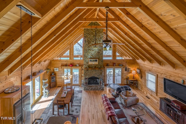 unfurnished living room featuring wood walls, wood finished floors, beam ceiling, and a stone fireplace