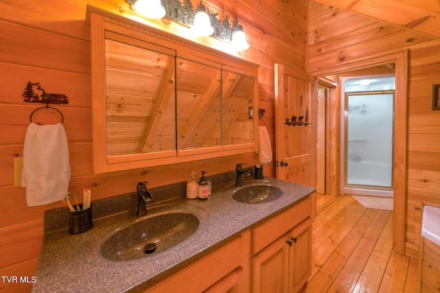 bathroom featuring wood walls, wood-type flooring, a sink, and a shower stall