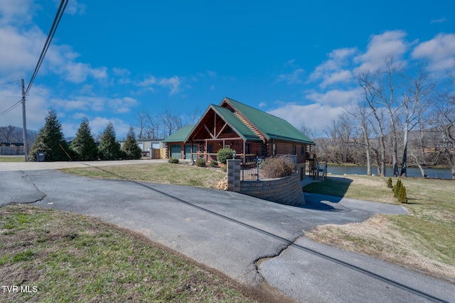 view of front facade featuring covered porch, metal roof, log exterior, driveway, and a front lawn