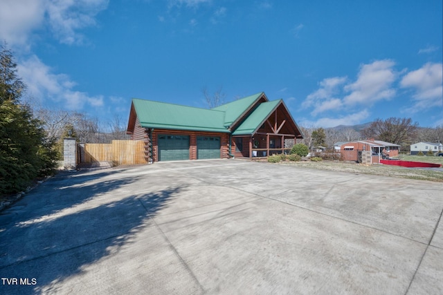 view of side of property with driveway, log siding, metal roof, an attached garage, and fence