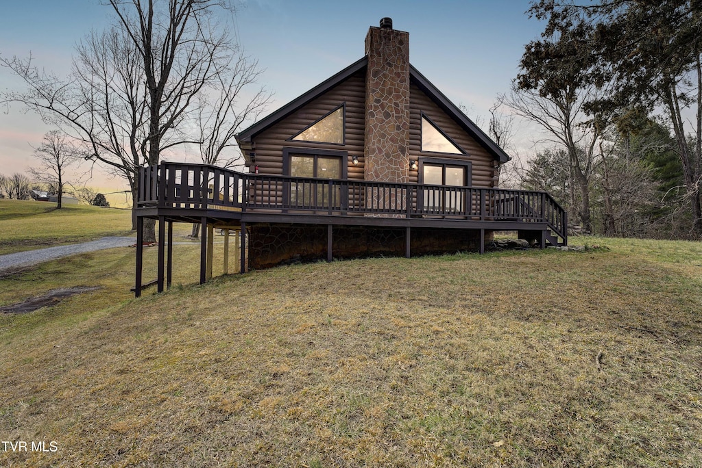 exterior space with a deck, a chimney, log siding, and a lawn