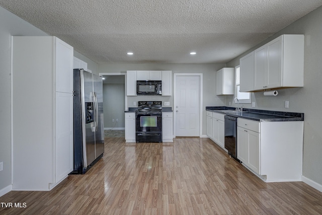 kitchen featuring dark countertops, light wood-style flooring, white cabinets, a sink, and black appliances