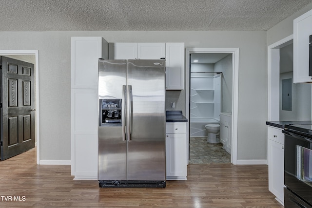 kitchen featuring black range with electric stovetop, wood finished floors, white cabinetry, dark countertops, and stainless steel fridge