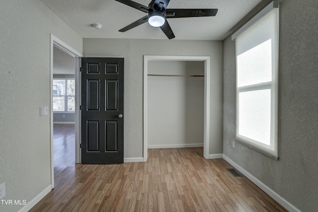 unfurnished bedroom with multiple windows, baseboards, wood finished floors, and a textured wall