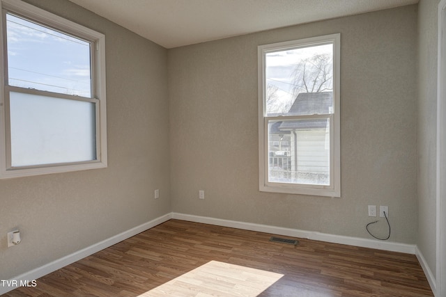 spare room with wood finished floors, visible vents, and baseboards