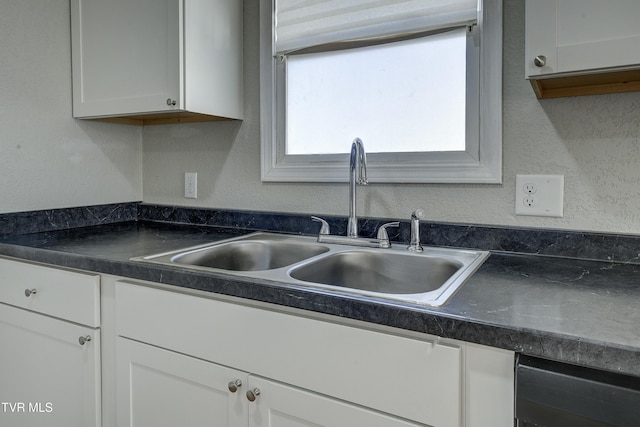 kitchen featuring dark countertops, white cabinets, a sink, and a textured wall